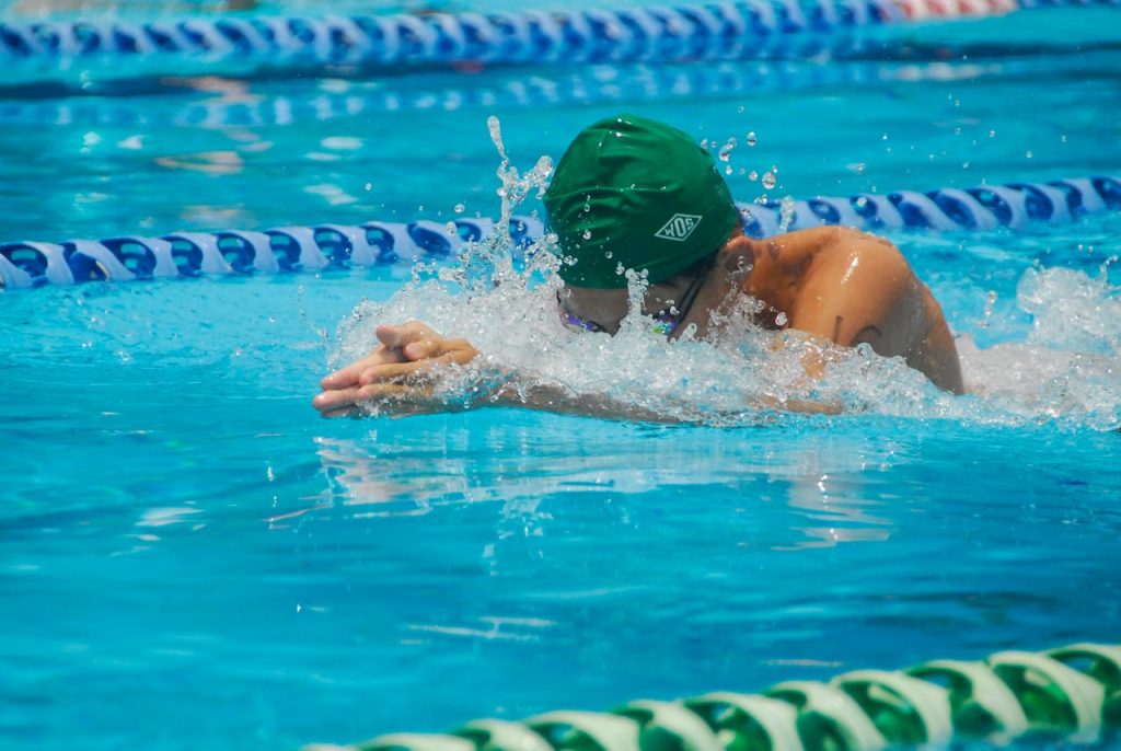 Focused swimmer in a pool during a race, featuring dynamic water splashes and vibrant turquoise water.